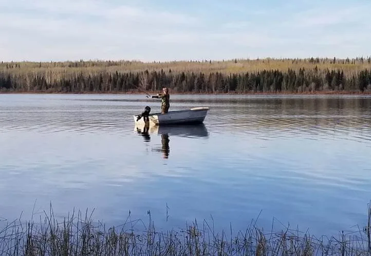 An angler standing and casting from a small boat on a mirror-calm lake at first light