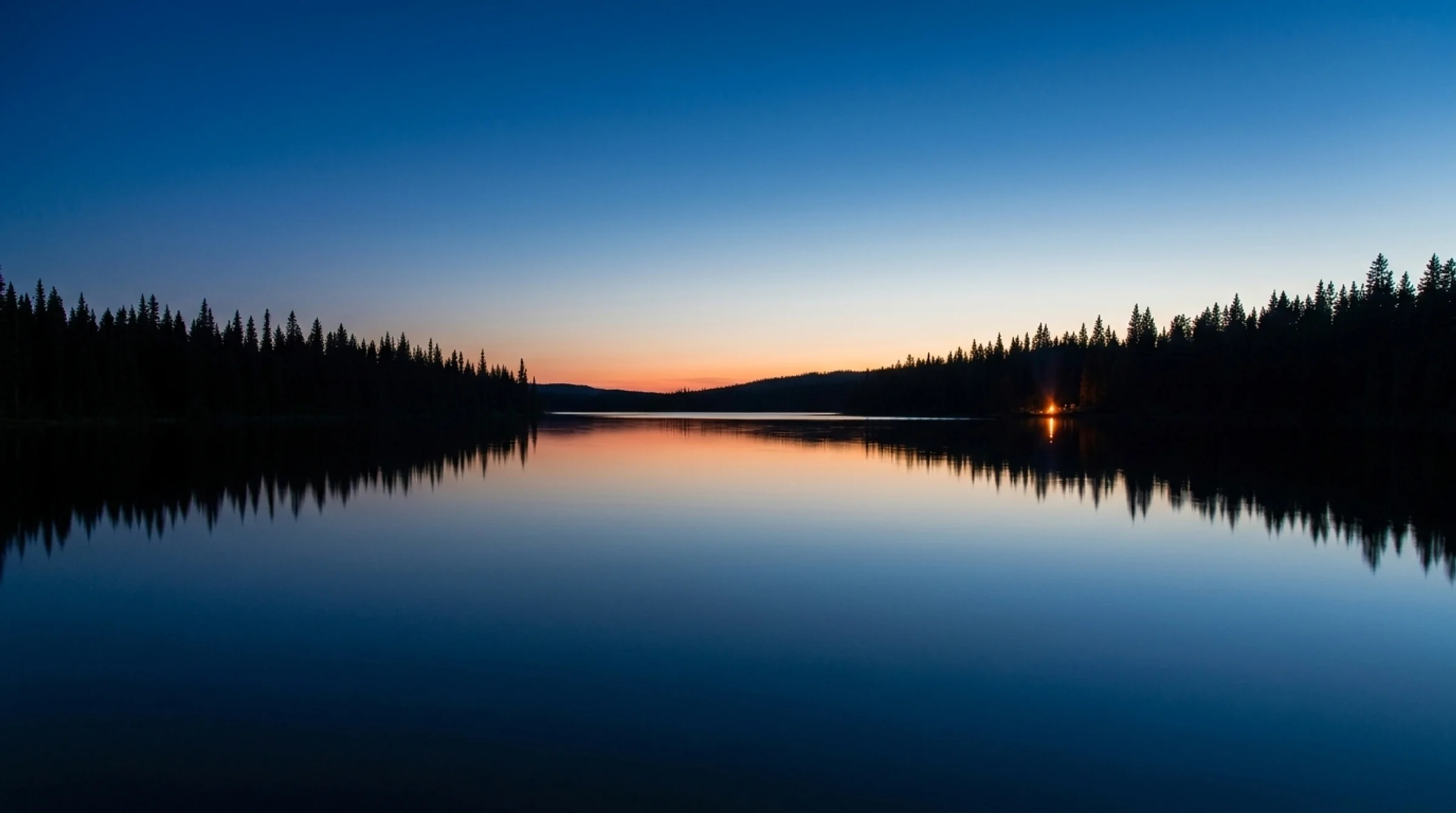 Twilight over a mirror-calm northern lake, dark spruce shorelines reflected in still water and a single campfire glowing on the far shore